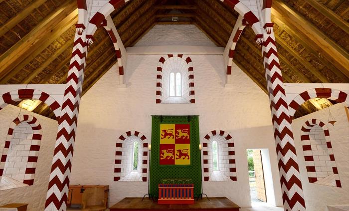 Inside a medievalprince's hall. the walls are white, there is red and white decoration painted around the tall arched windows and timbers supporting t